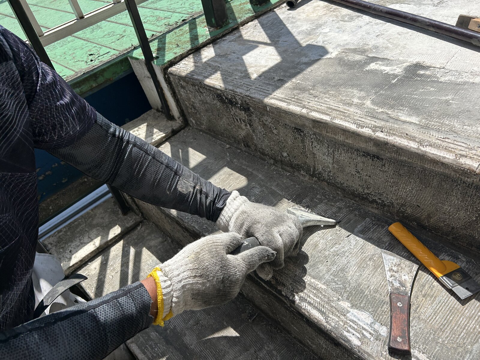 スクレイパーを使ったケレン作業で下地に残った旧接着剤を削り取る様子