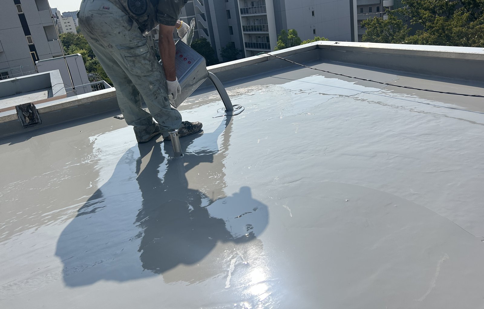 屋上にウレタン防水材を流して塗り広げる作業